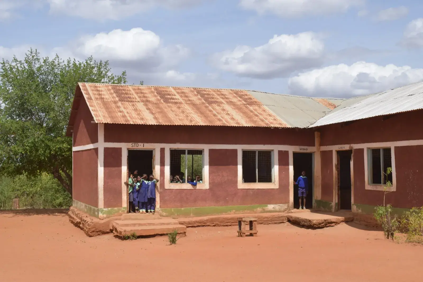 A single-storey rural school with red walls and a tin roof on red earth