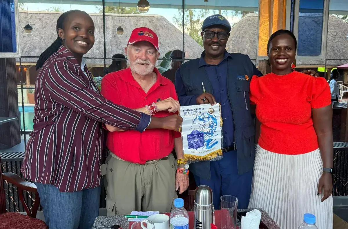 Four adults standing together at a restaurant table: a woman in a striped top, an older man in a red cap, a man in a dark shirt and a woman in a red top