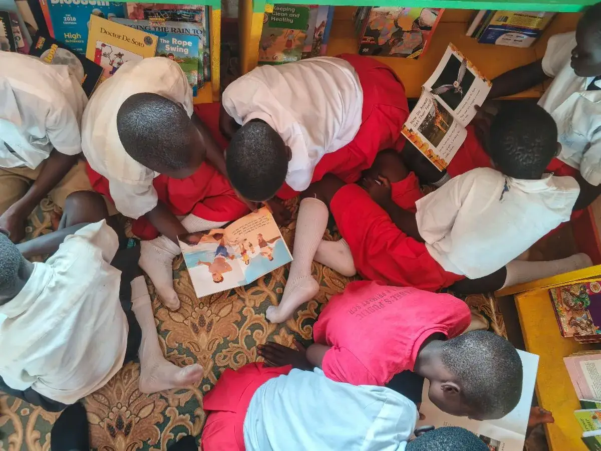 Pupils in red and white uniforms crouched over books on the floor of a library, seen from above