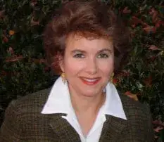 Millie West, the author, smiling in a tweed jacket and white collar, in a portrait
