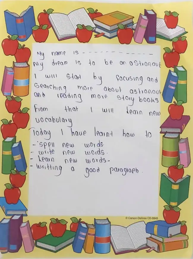 A student's handwritten note on paper bordered with drawings of books and apples, stating a dream to be an astronaut and listing new words learnt