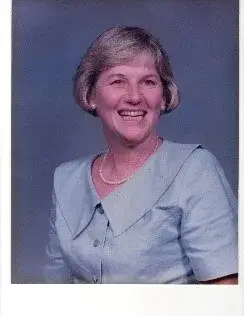 A smiling woman with short fair hair in a pale blue collared top, in a studio portrait