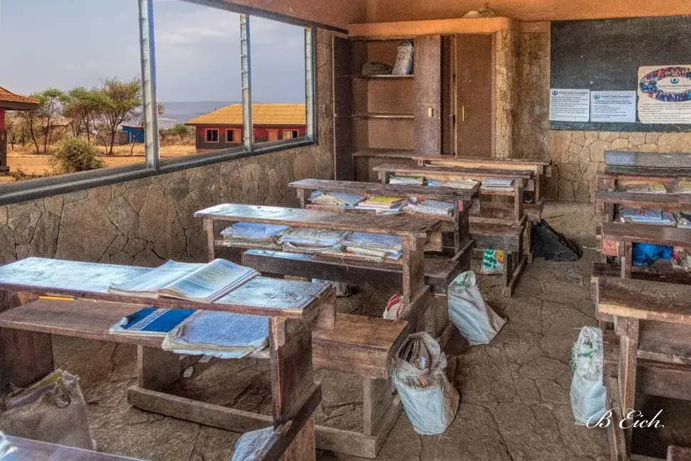 A bare classroom at Amboseli Primary School with open windows and plastic-bag schoolbags on the desks