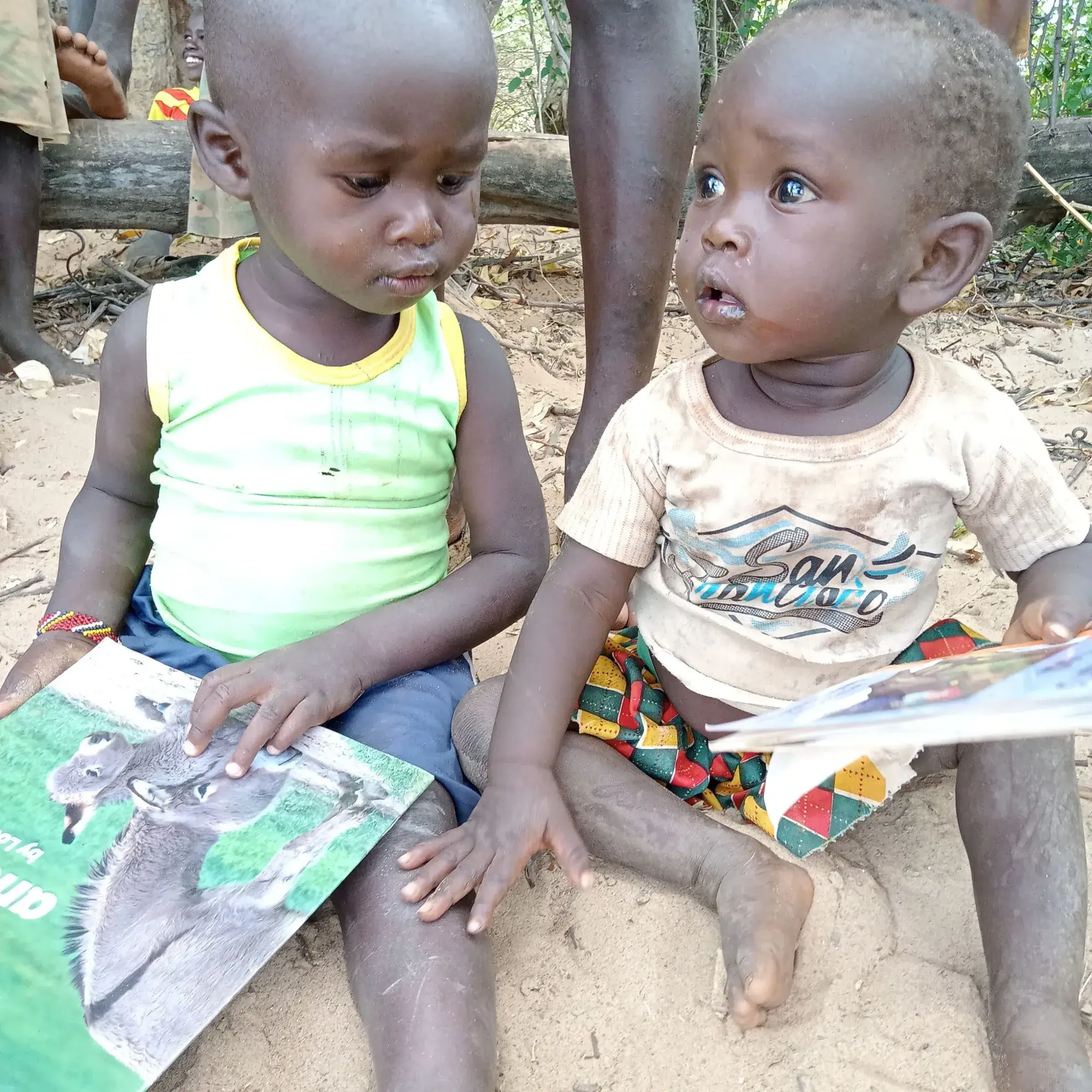 Two small children sitting on the ground with picture books on their laps