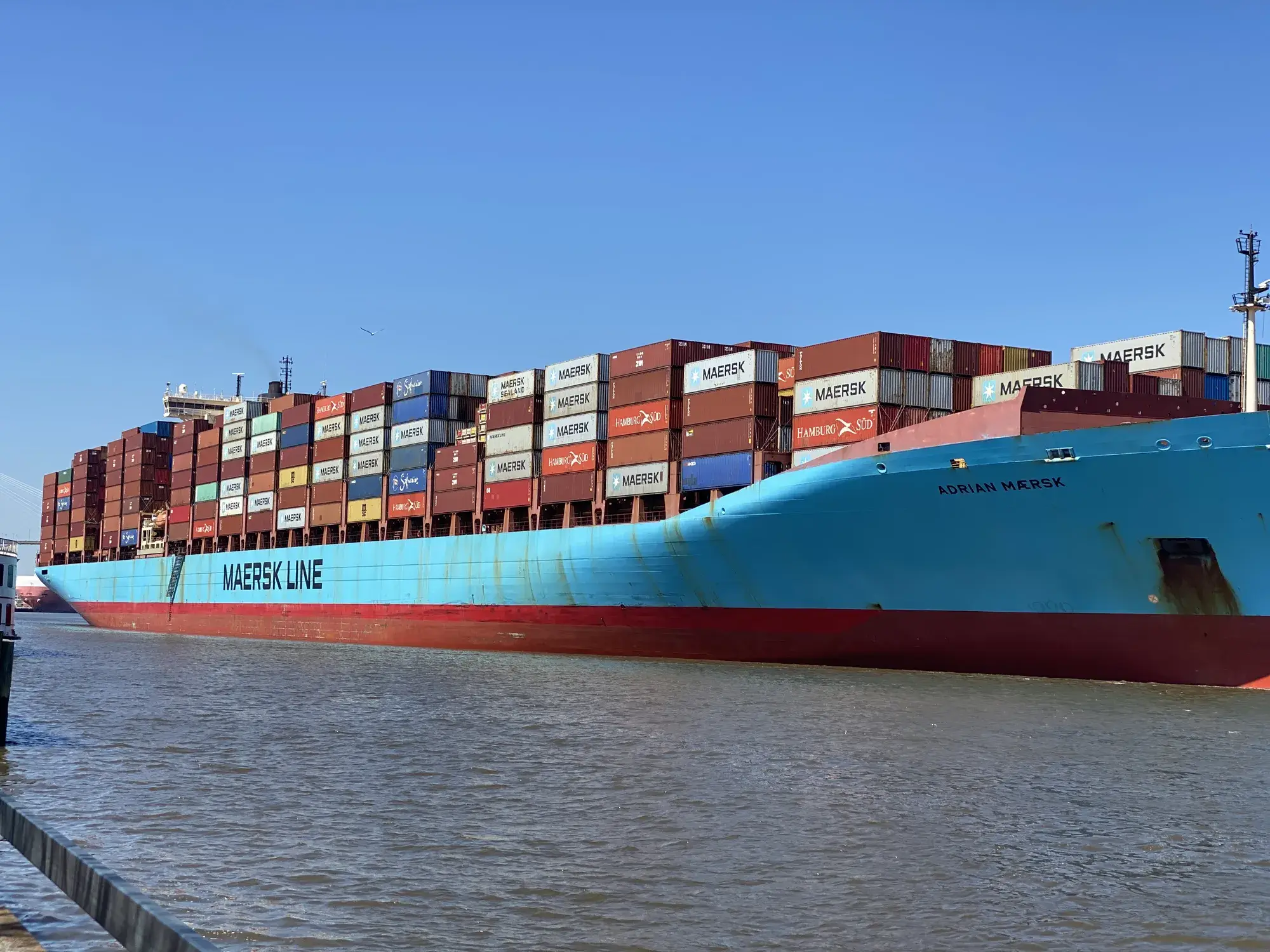 A Maersk container ship stacked with containers on a river