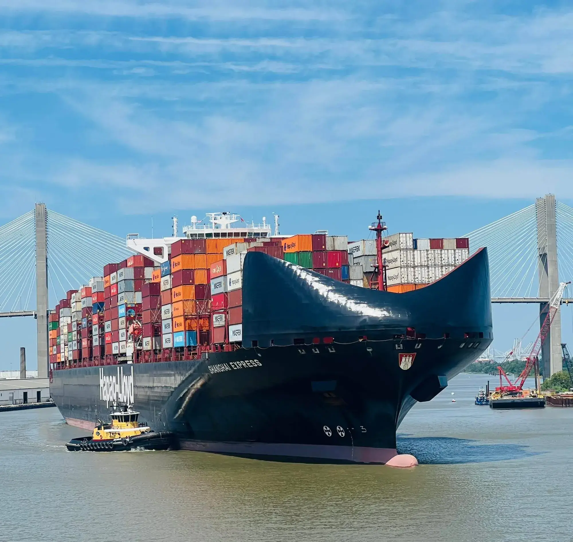 A container ship guided by a tug under a cable-stayed bridge